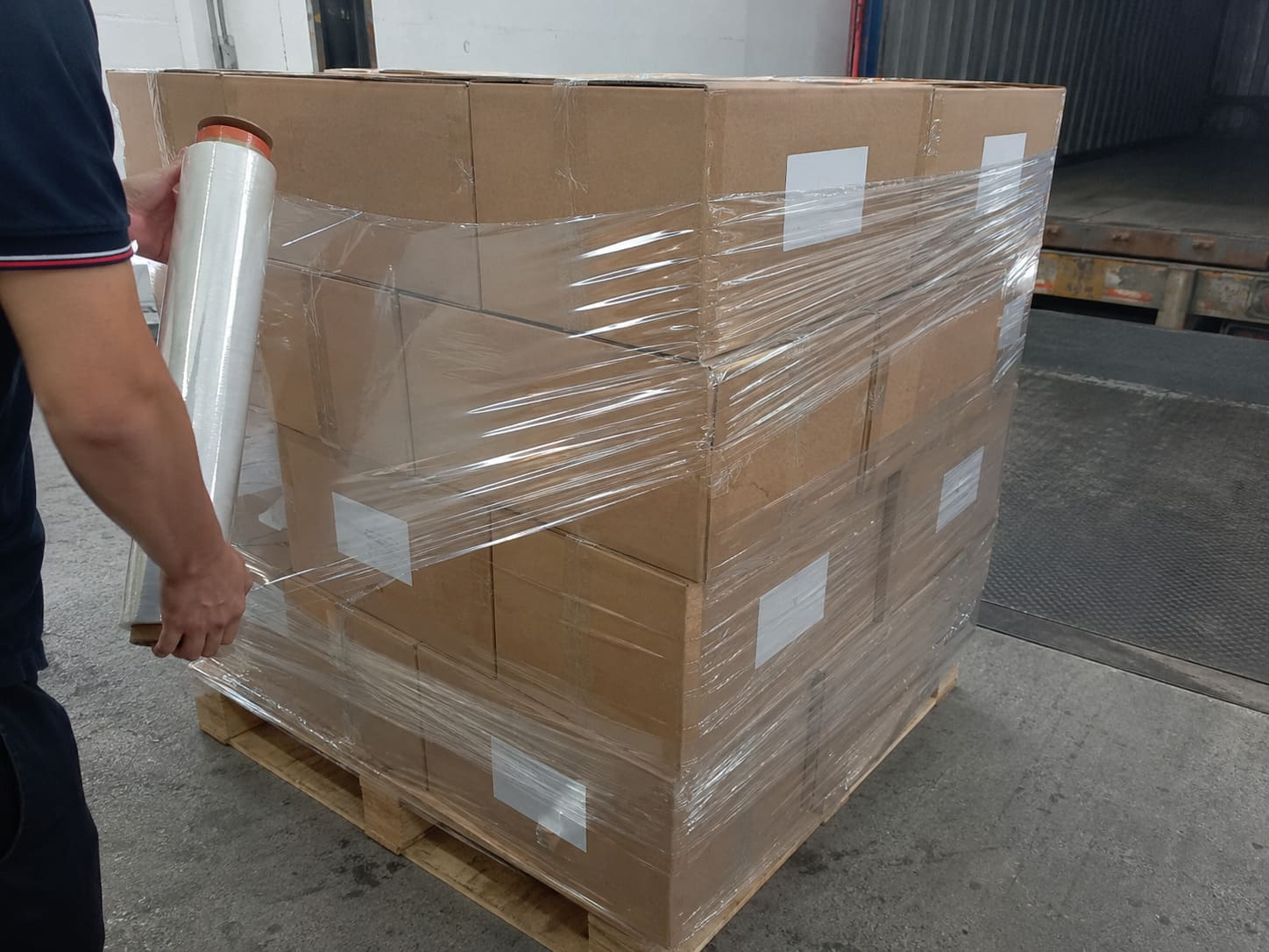 Warehouse shipping scene with stacked export cartons on pallets and goods being loaded into a container for international delivery